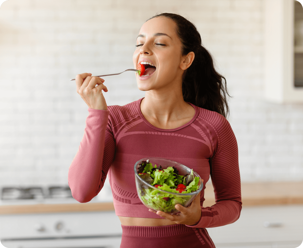 Woman enjoying salad in a kitchen.