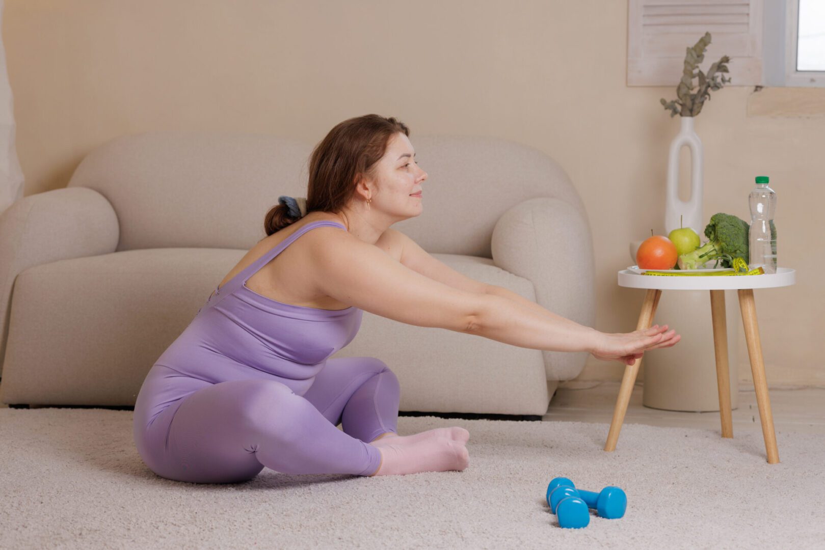 Woman stretching on carpet near dumbbells.